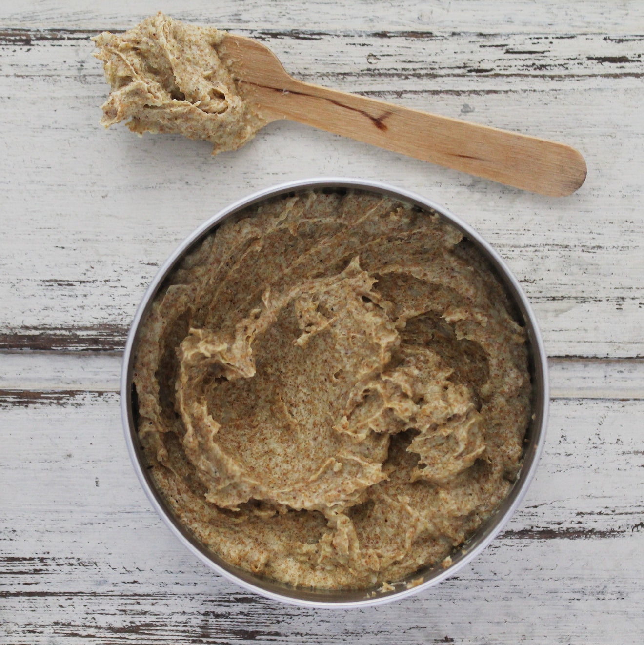 Brown speckled scrub in aluminium jar on whitewashed wooden background