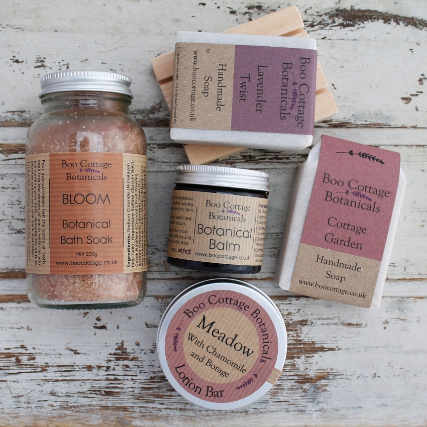 Botanical gift box contents, with soaps, bath soak and balms on whitewashed wooden background