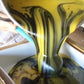 Yellow and black streaked soap batter being poured from big saucepan into white mould