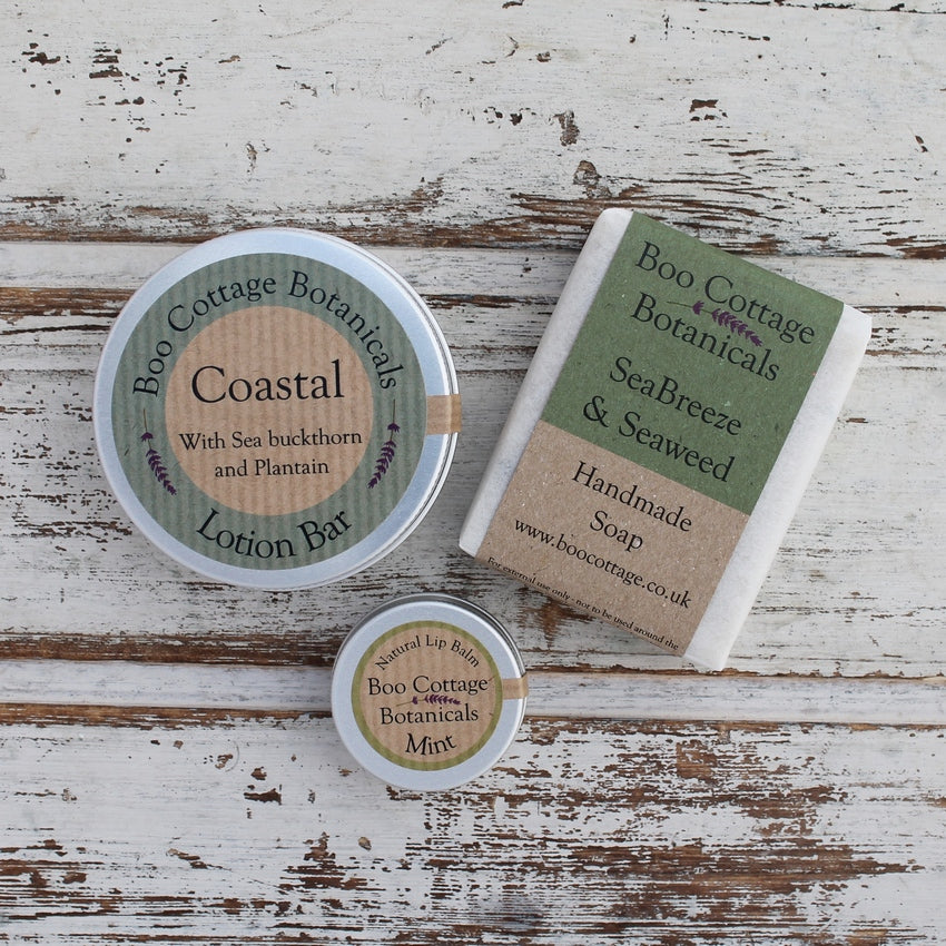 Round aluminium lotion bar tin, soap bar wrapped in green card, small aluminium lip balm tin on whitewashed background