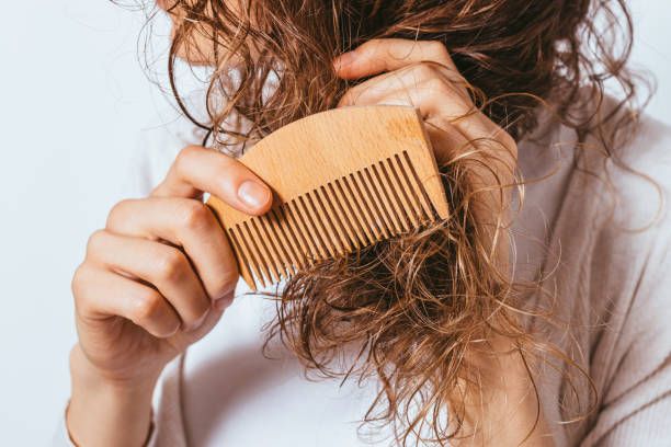 Wet curly hair being combed with wooden comb