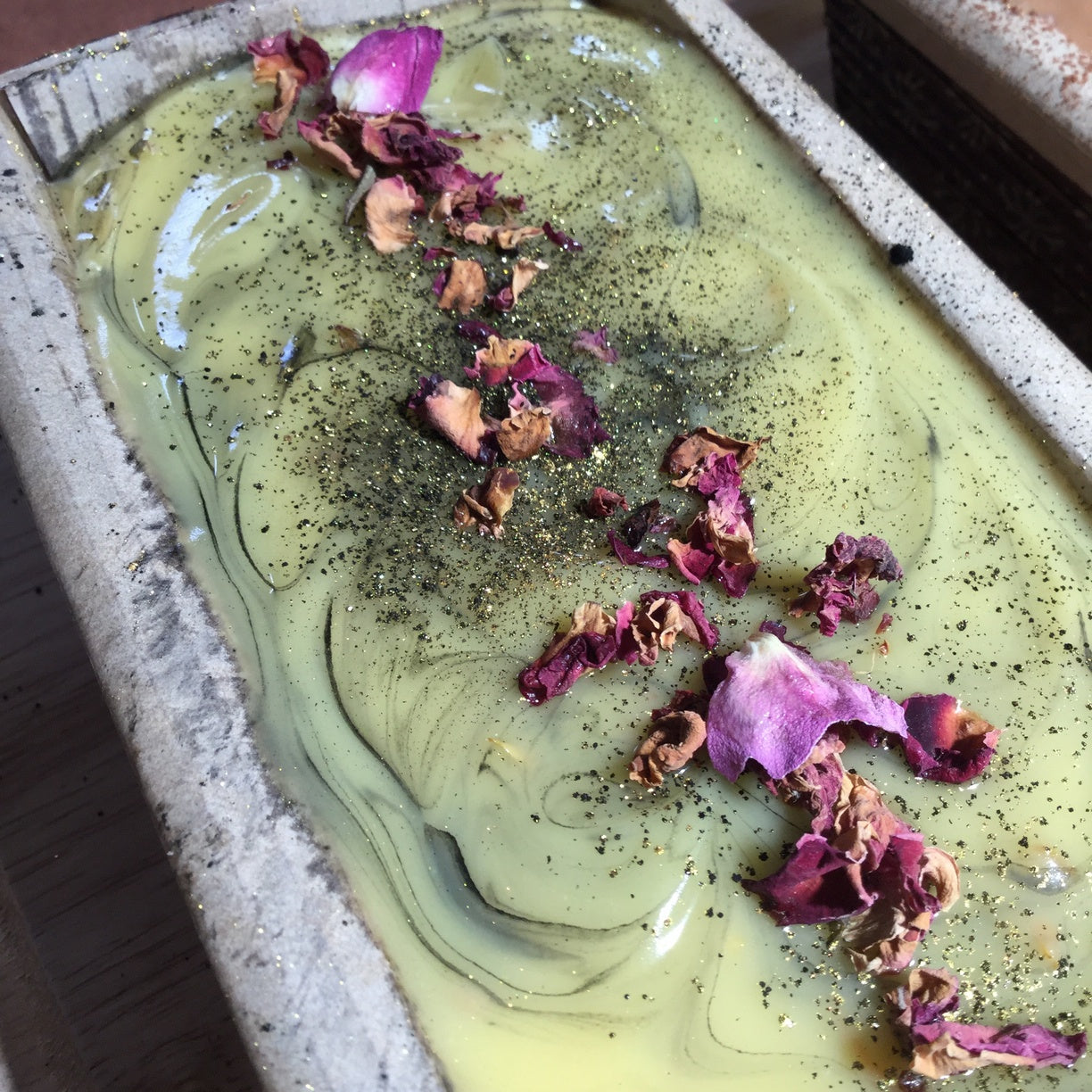 Cream soap with black streaks and rose petals on top in cardboard mould