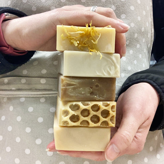 A person holding five different soap bars, with one bar topped with calendula petals.