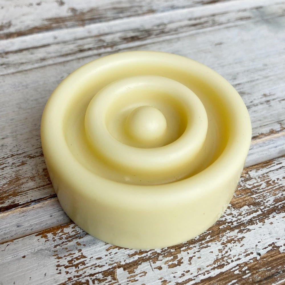 Cream coloured solid lotion bar with concentric ring design on whitewashed background