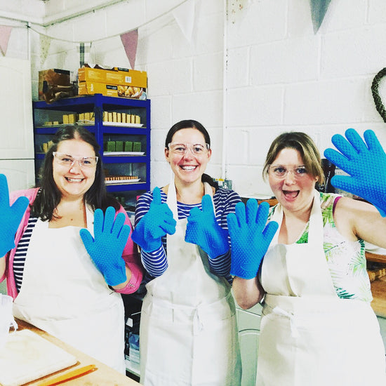 3 smiling students with cream aprons and blue silicone oven gloves 