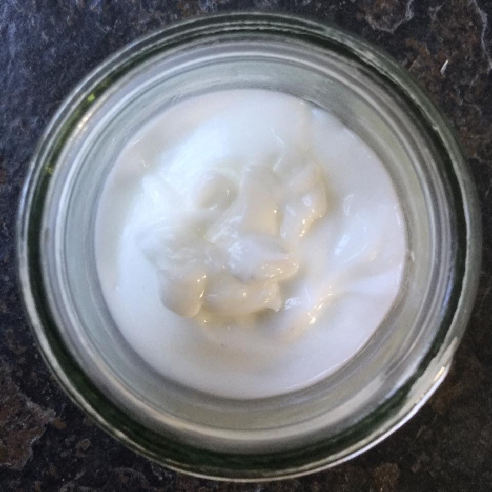 White lotion in glass jar on slate background