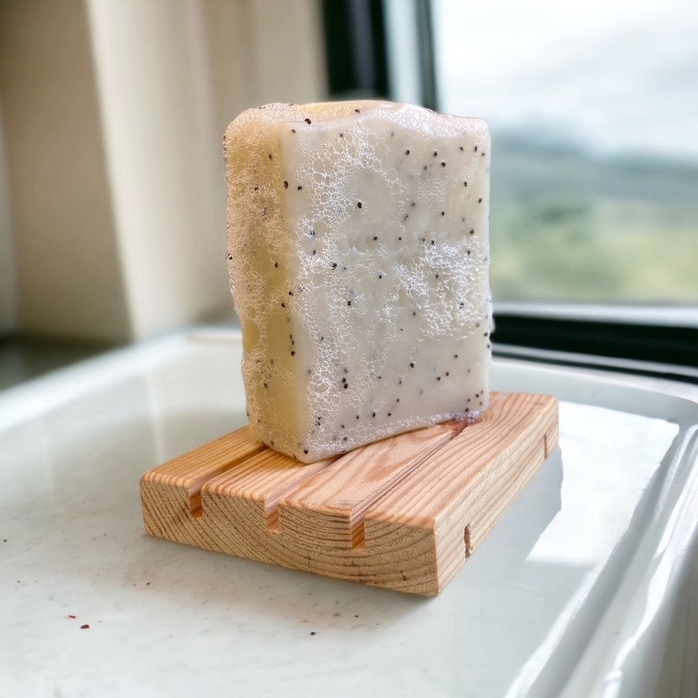 Cream coloured juniper scrub soap with poppyseeds stood up on natural soap dish