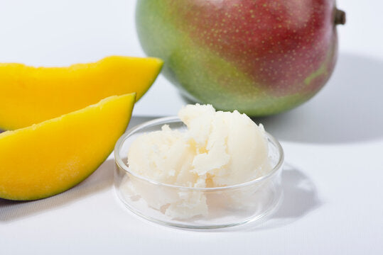 Clear glass dish with cream mango butter with slices of mango and whole mango in background on white counter