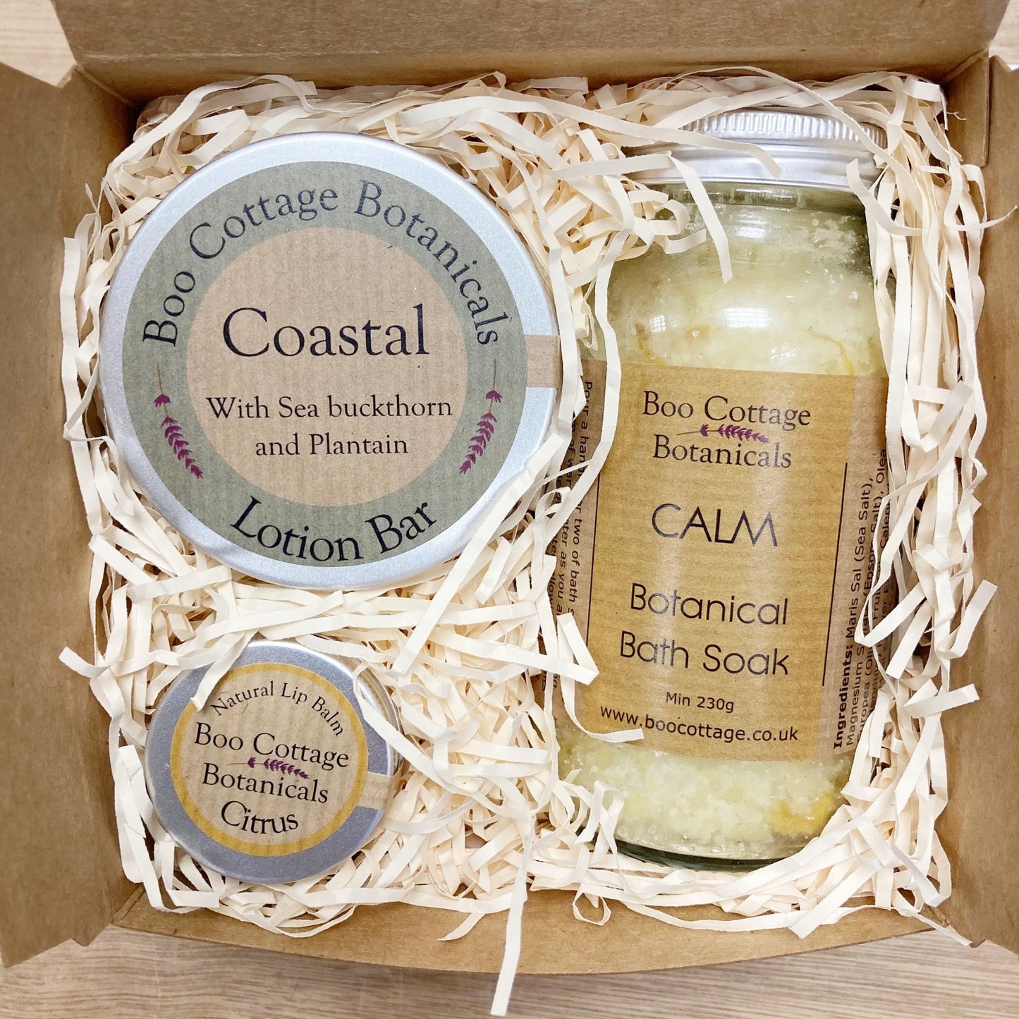 Open gift box showing a Coastal Lotion Bar, A CALM Bath Soak and a Citrus Lip Balm with shredded cream paper