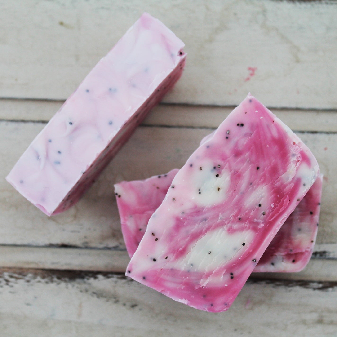 Pink and white swirled soap bars with poppy seeds on whitewashed background