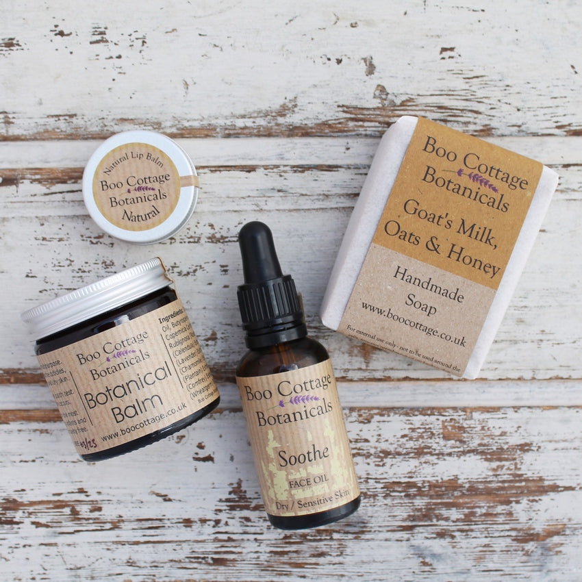 Amber jar and bottle with black dropper pipette, small aluminium tin and soap bar all with brown labels on whitewashed wooden background