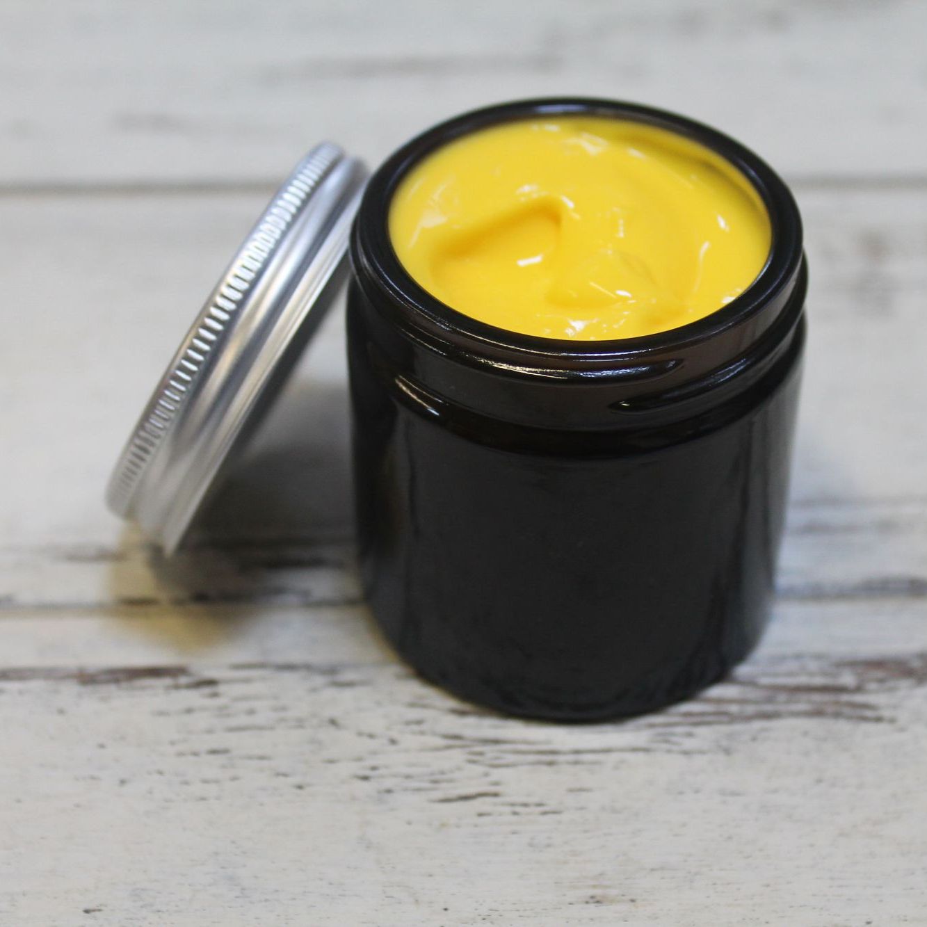 Yellow lotion in amber jar with whitewashed wooden background