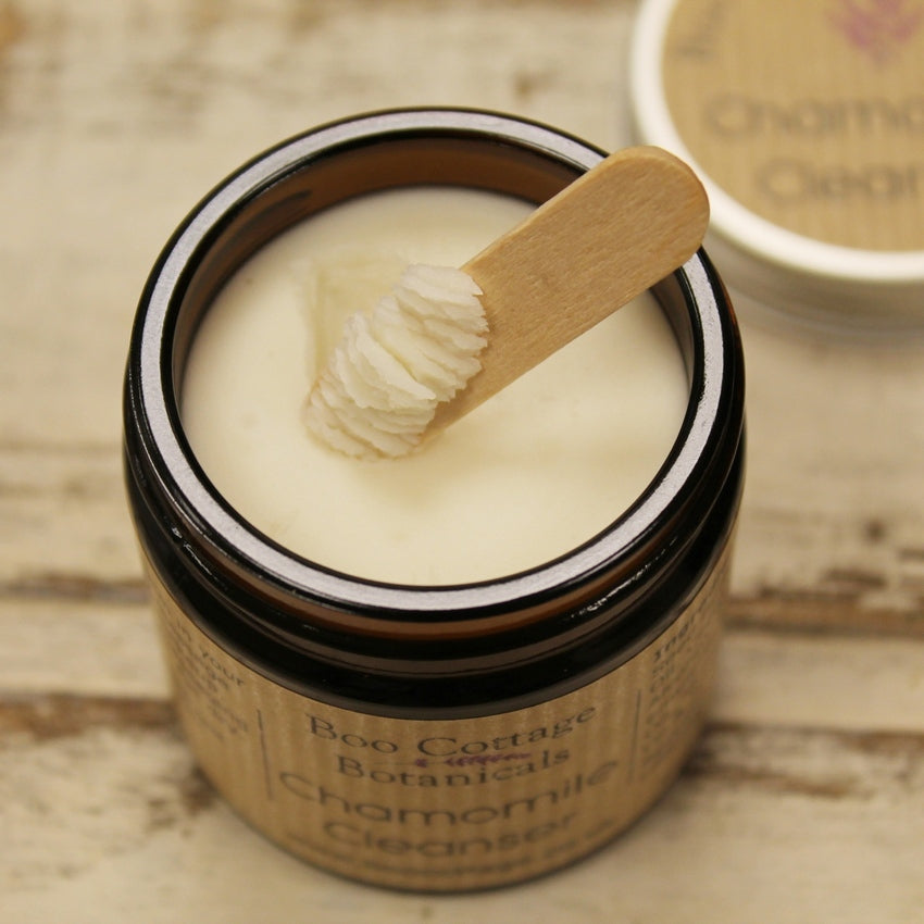 White balm in amber glass jar being scooped by a wooden spatula with whitewashed wooden background