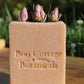 Pink soap bar with rose buds on top on wooden table with green outdoor background