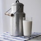 Vintage aluminium milk carrier and glass of milk on striped cloth with white background
