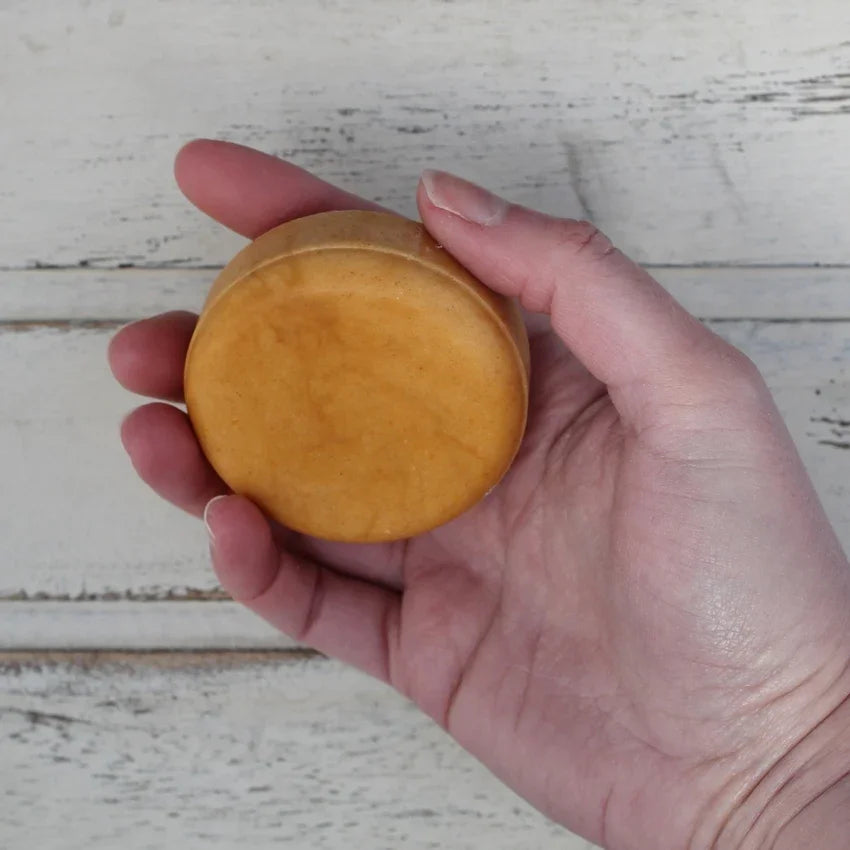 Flat round orange shampoo bar in white female hand on whitewashed wooden background