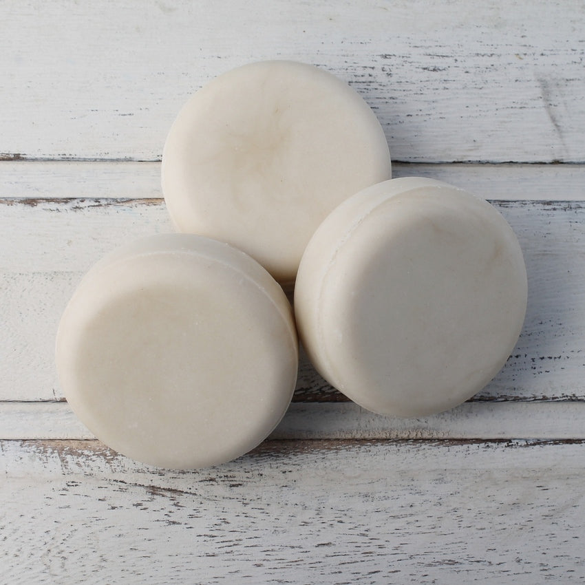 Pile of three cream flat round shampoo bars on whitewashed wooden background