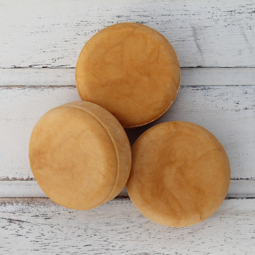 Pile of three flat round orange shampoo bars on whitewashed wooden background
