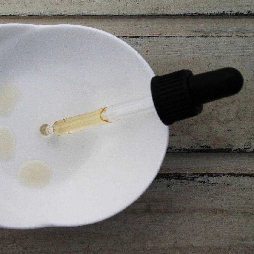 Pale oil in pipette with black dropper dropping oil into white dish