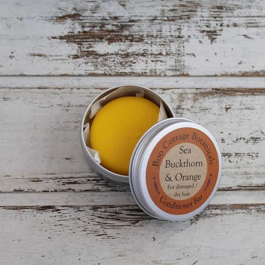 Orange round solid conditioner bar in aluminium tin on whitewashed wooden background