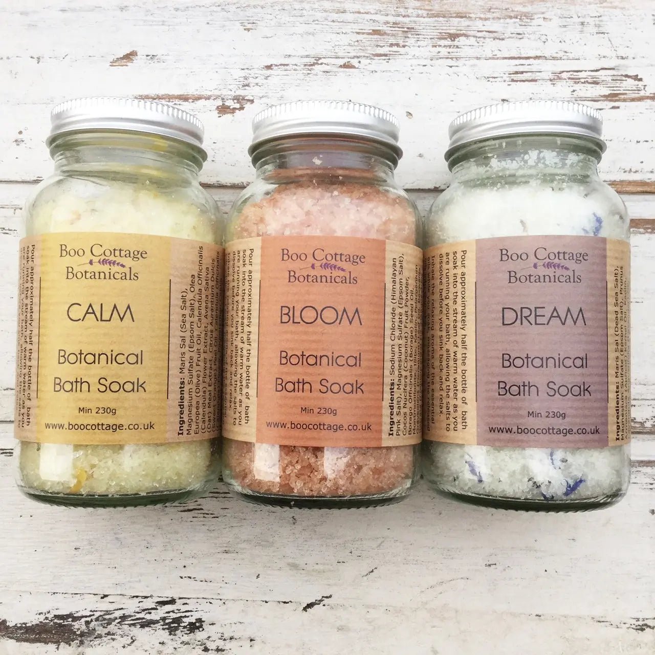 Line of 3 bath soaks with coloured salts in clear glass bottles on white wooden background