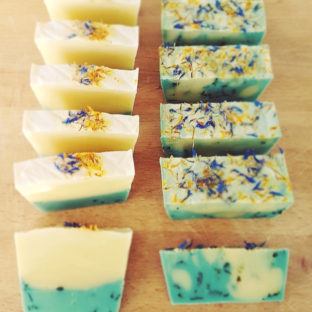 Cream and green bars of natural handmade soap lined up on chopping board