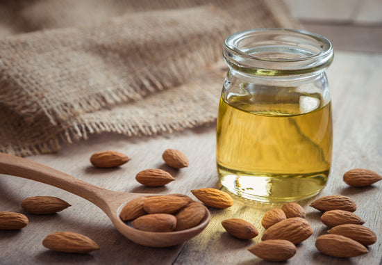 Golden oil in glass jar with almonds and spoon in foreground
