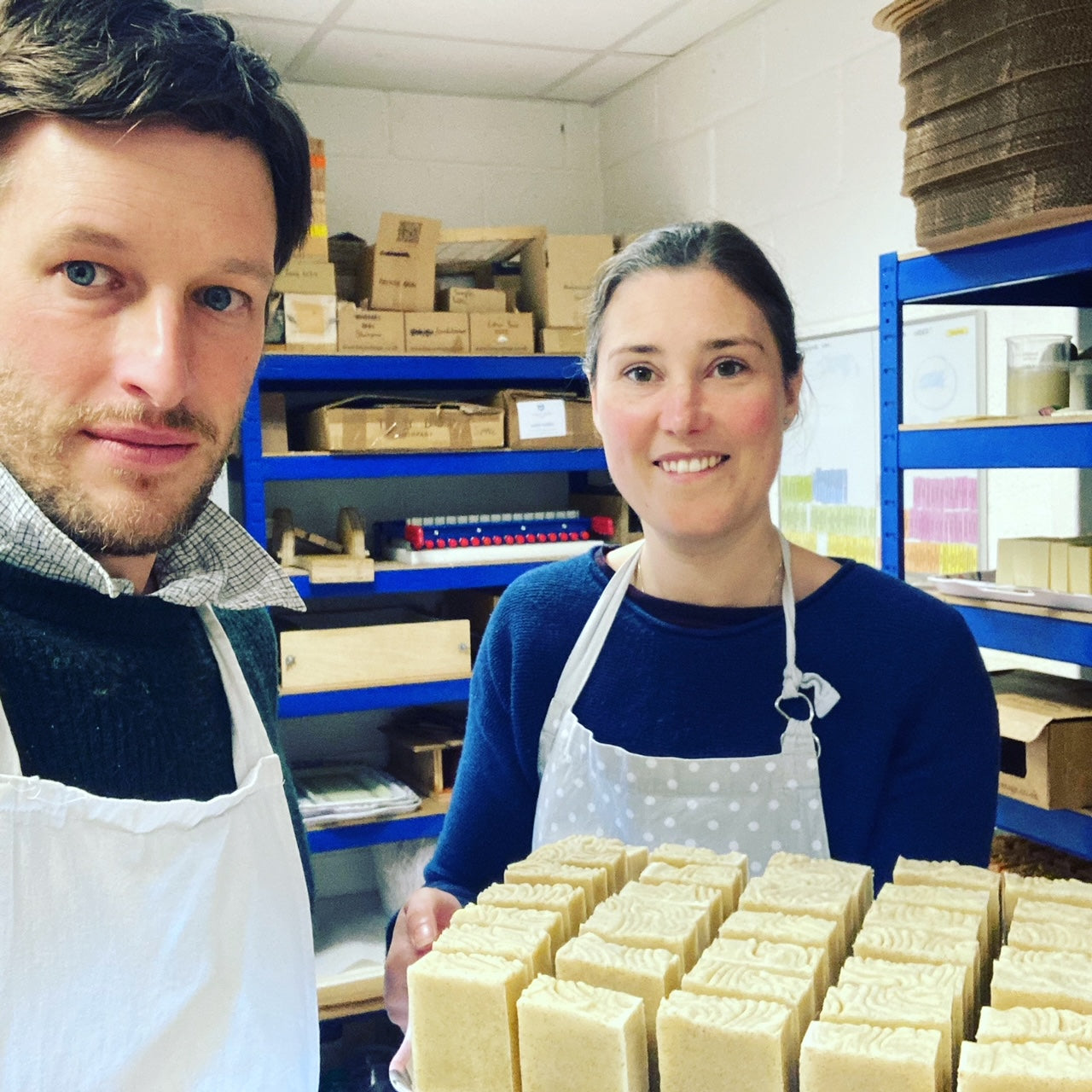 Smiling white brunette male and female with aprons on holding tray of cream coloured soap bars