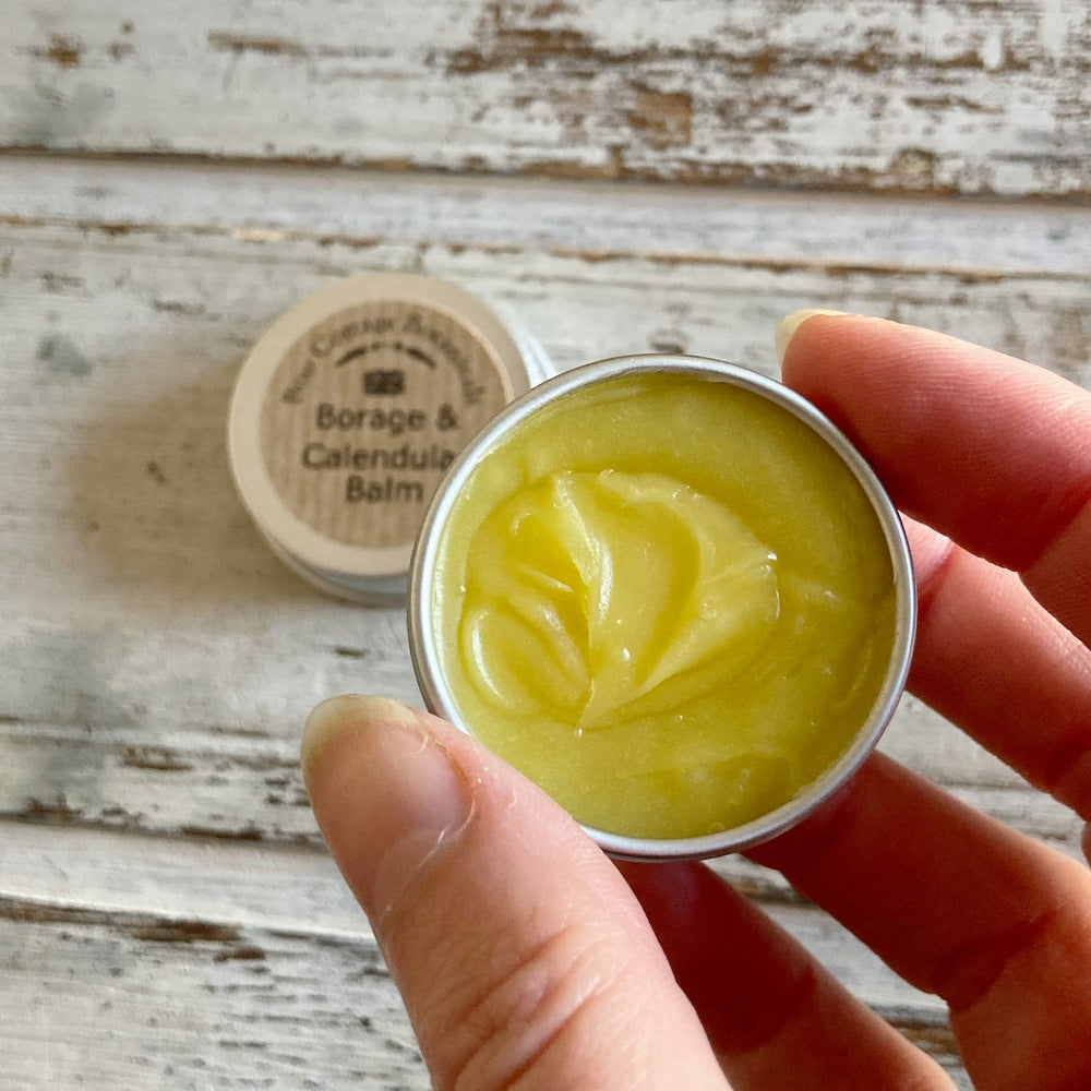 Yellow Borage & Calendula balm sample in mini aluminium tin in hand against a white background