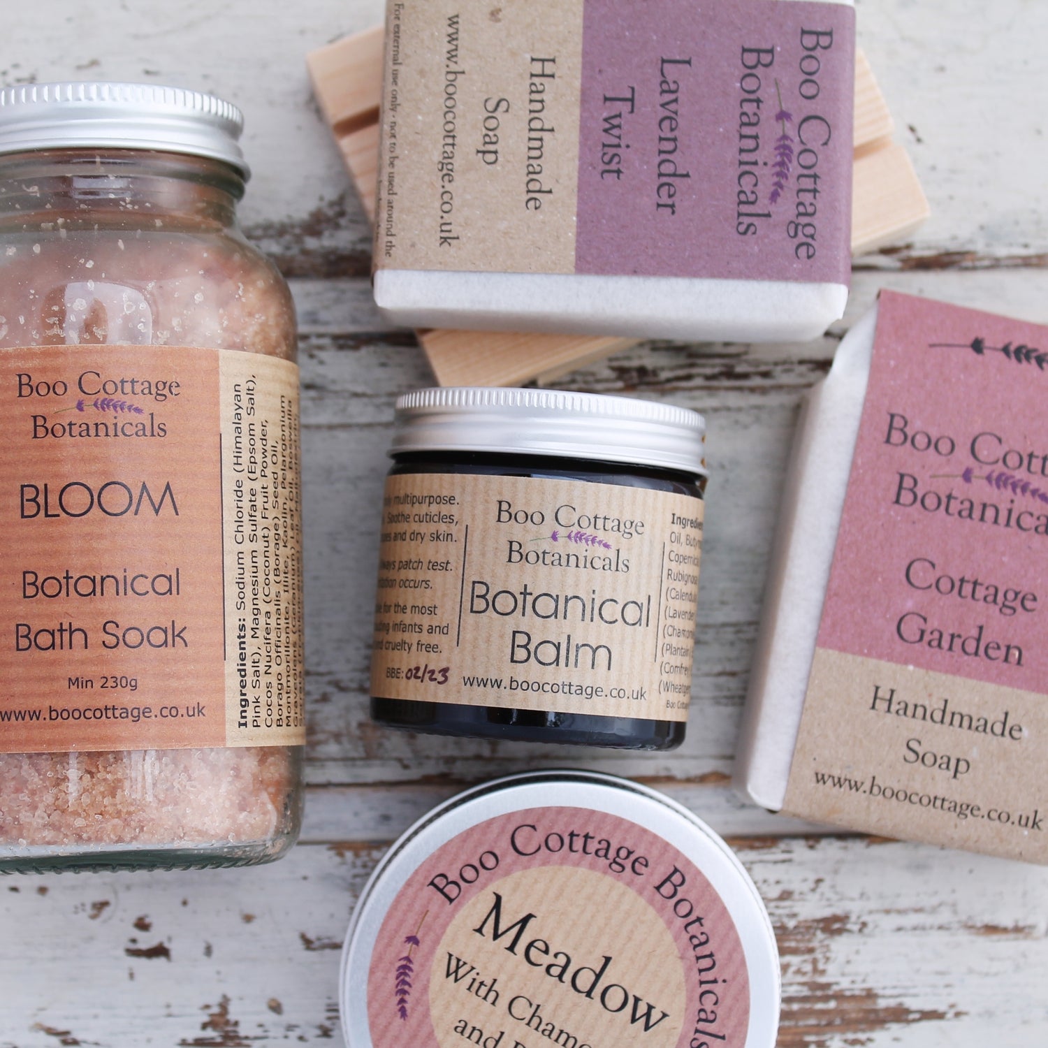 Collection of botanical products with pink and purple labels in glass jars and tins on white wooden background
