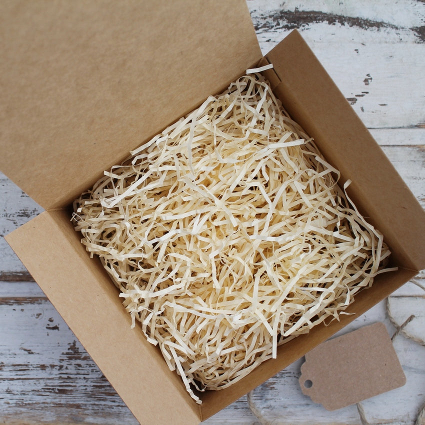 Open brown gift box with cream shredded paper with card tag, jute string on whitewashed wooden background