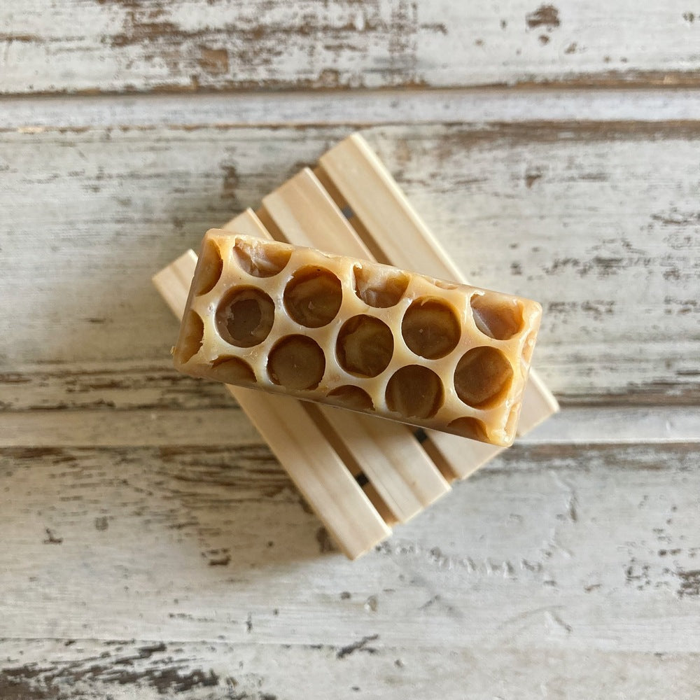 Overhead view of honeycomb top of brown soap on wooden soap dish on whitewashed wooden background