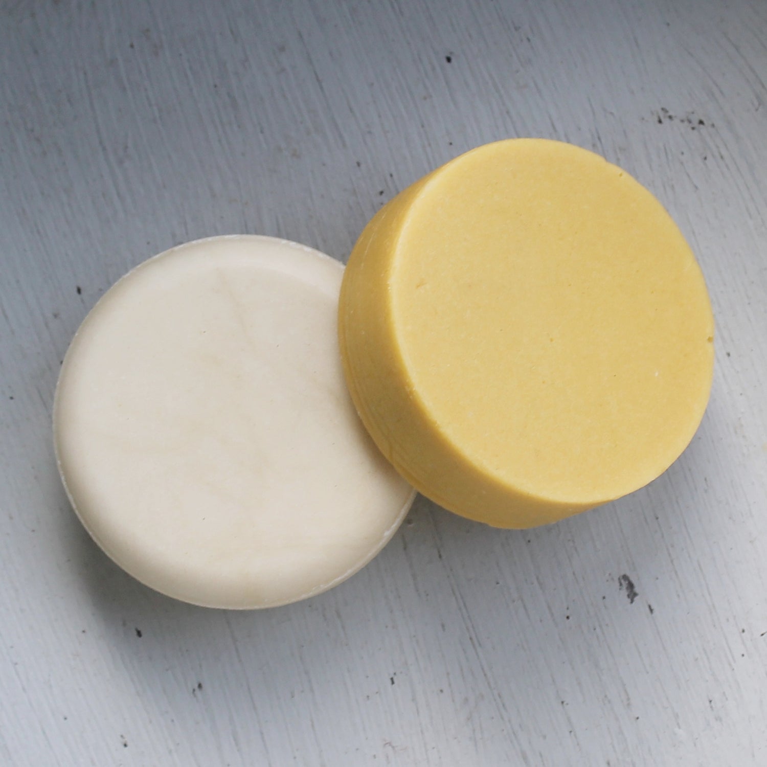 Flat round cream shampoo bar and orange conditioner bar on white background
