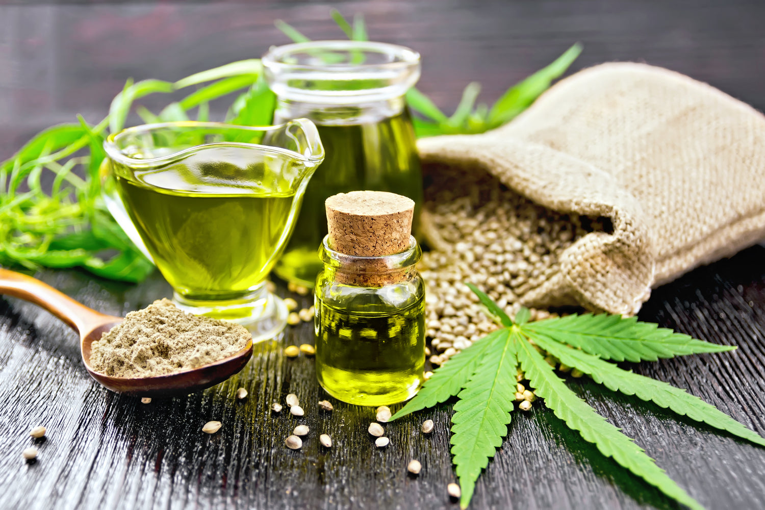 Hemp oil, powder and leaves on black wooden background