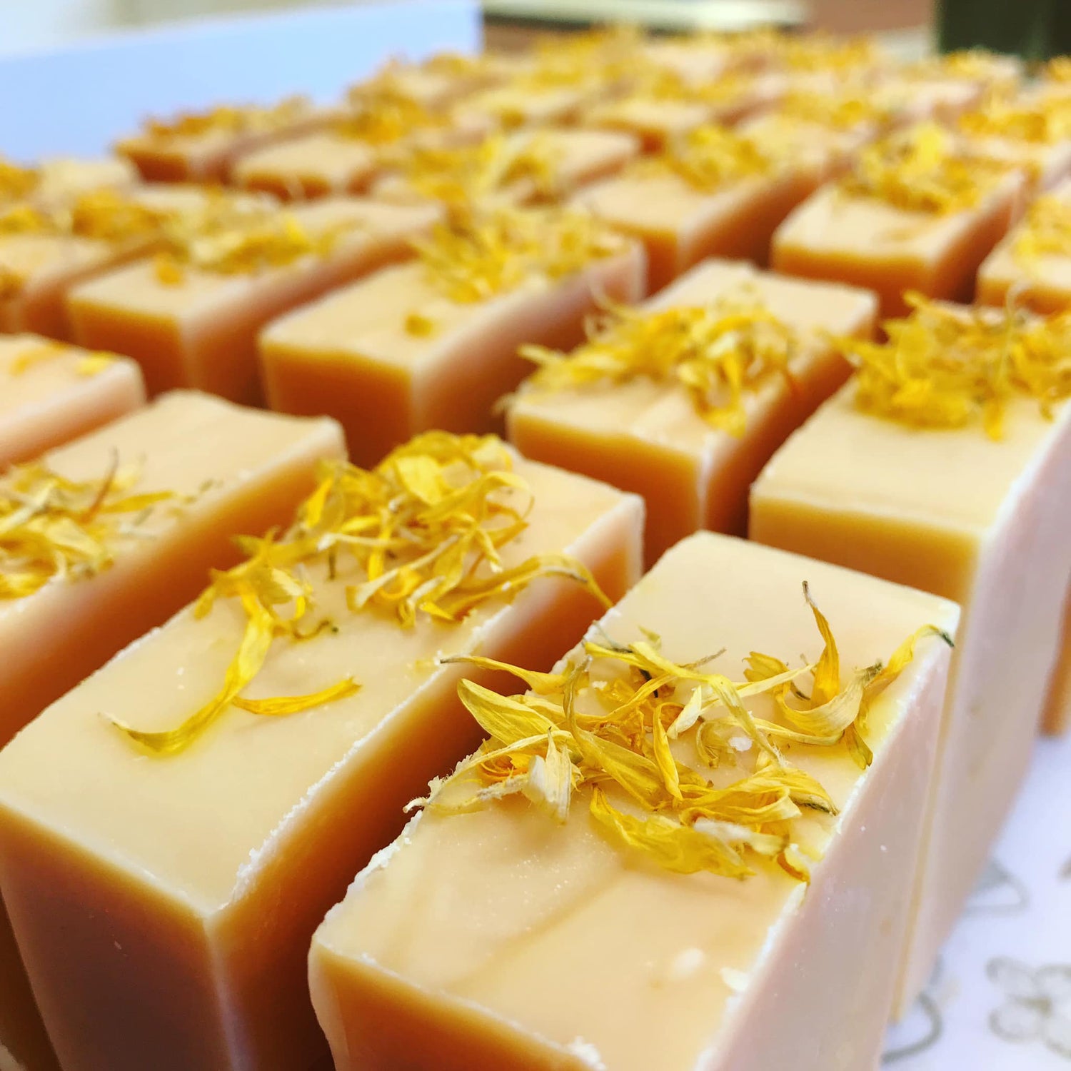Collection of yellow bars of soap with calendula petals on top all uniform, lined up next to each other