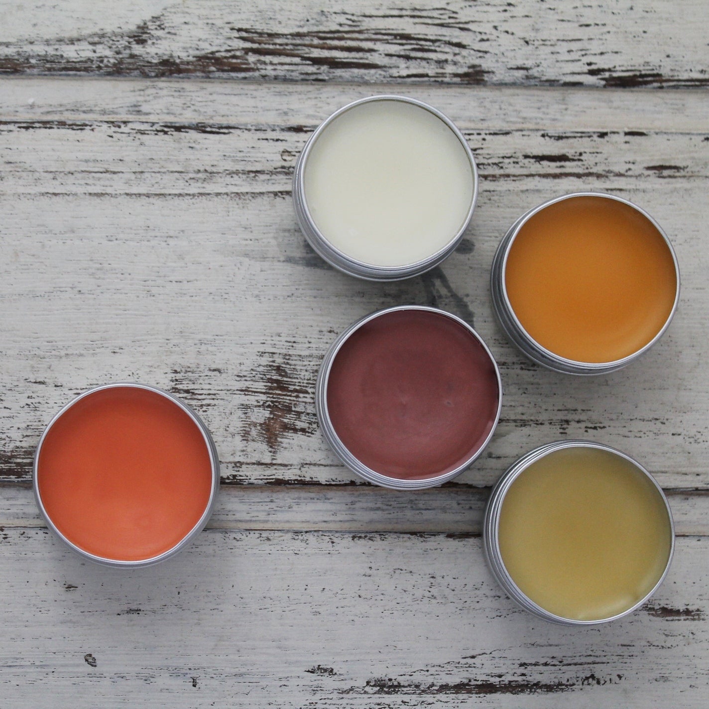 Multicoloured lip balms in tins on whitewashed wooden background