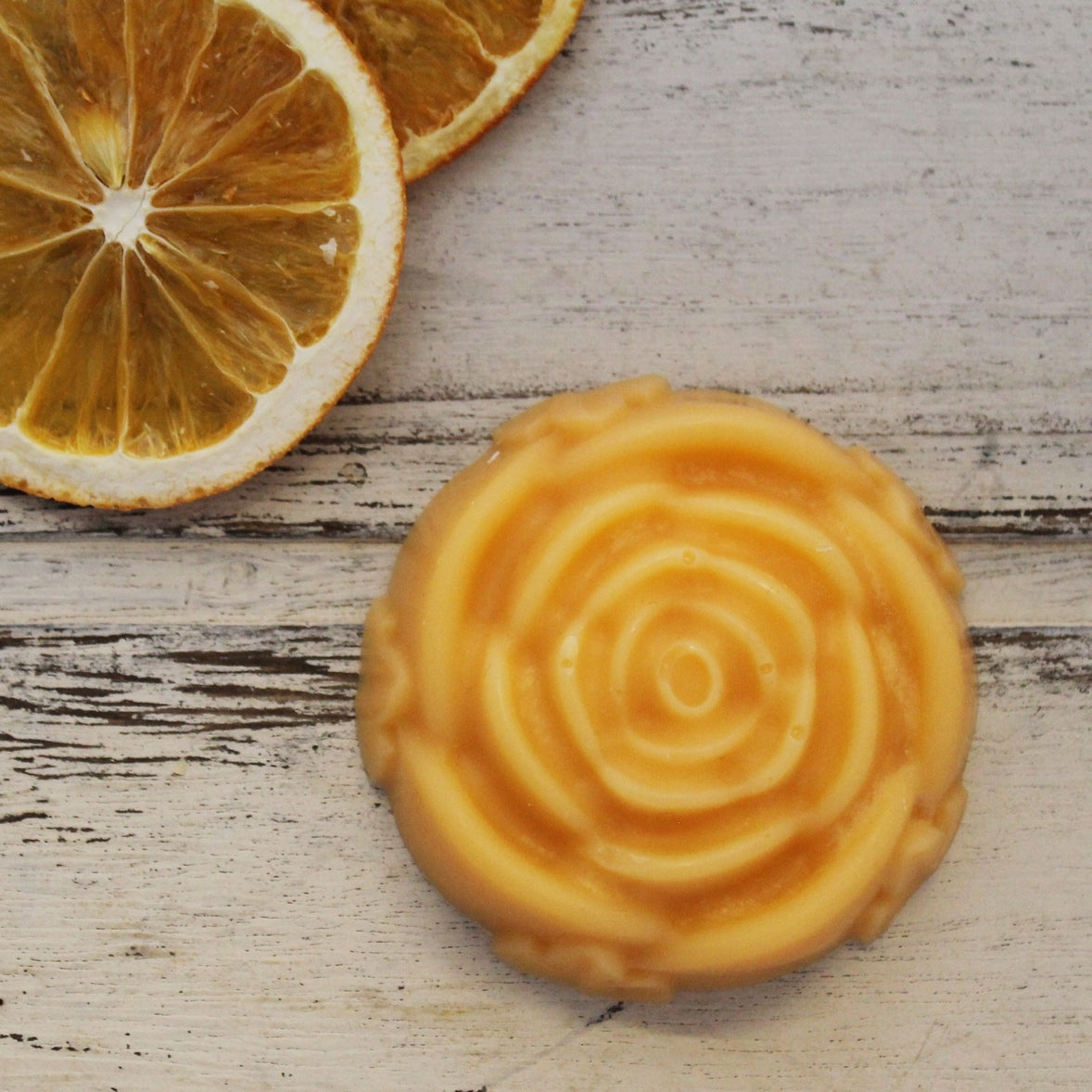 Orange floral lotion bar with dried oranges on whitewashed wooden background
