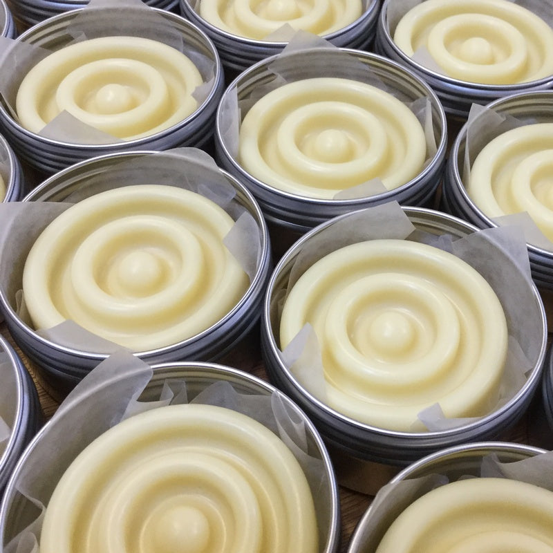 Collection of cream round lotion bars in tins next to each other