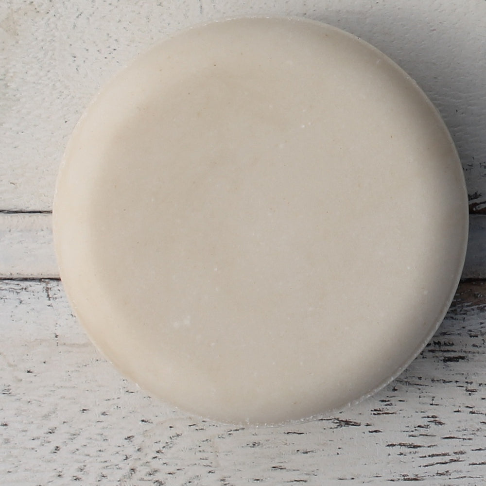 Close up of cream round shampoo bar on white wood background