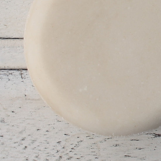 Close up of cream round lotion bar to show smooth texture on white wood background