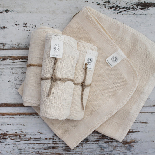Pile of cream cotton face cloths with organic labels tied with jute string on whitewashed wooden background