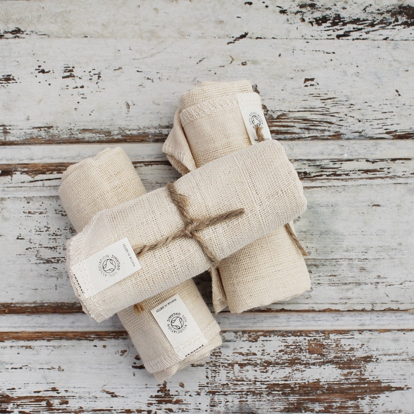 Pile of three rolled cream face cloths with organic labels tied with brown string on whitewashed wooden background
