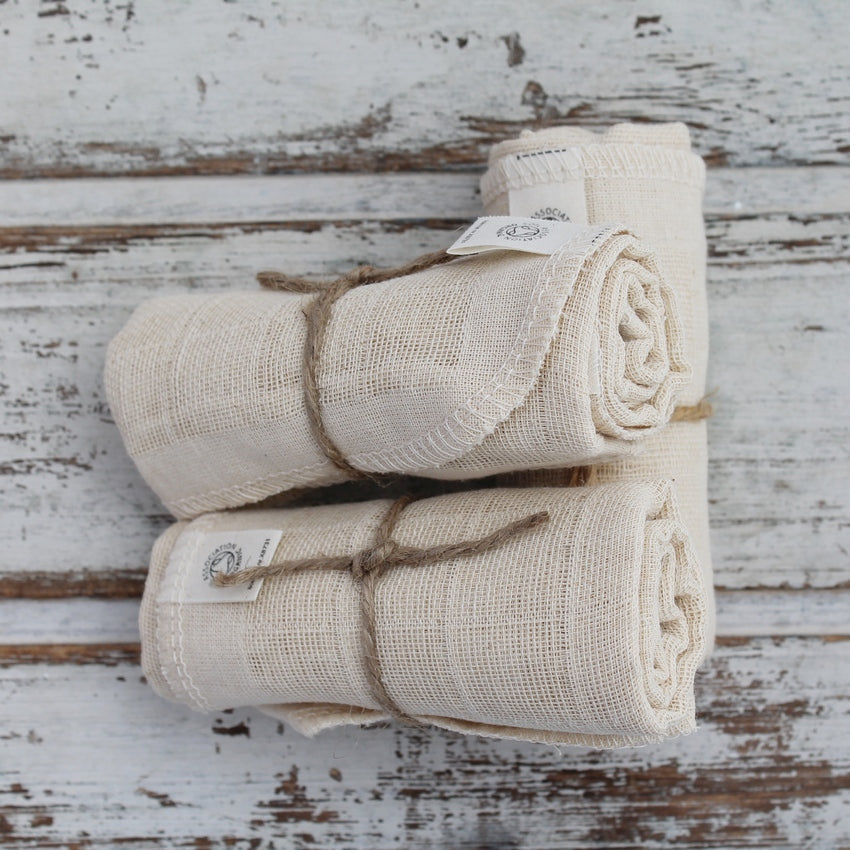 Pile of three rolled up cream organic cotton wash cloths on whitewashed wooden background