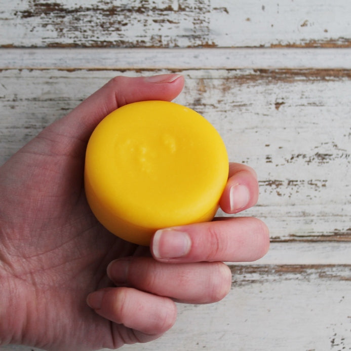Round yellow-orange conditioner bar in hand