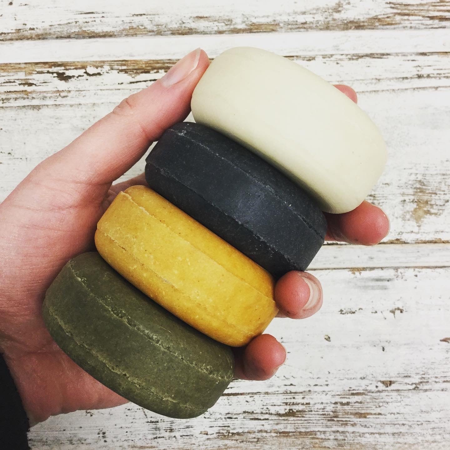 4 natural coloured shampoo bars in hand with whitewashed wooden background