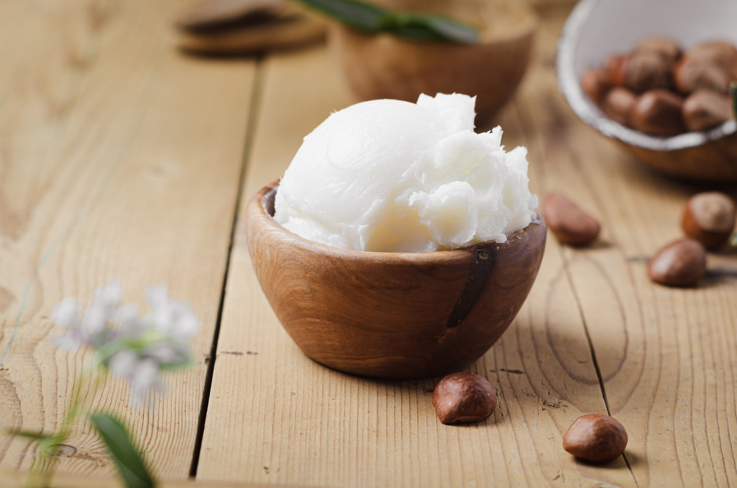 Creamy butter in wooden bowl with shea nuts on wooden background