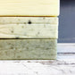 Cream, pale green and natural flecked green soap bars stacked on top of each other on white wood background