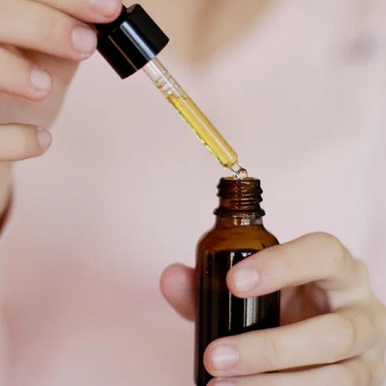 Female hands holding amber bottle with clear pipette with golden coloured oil