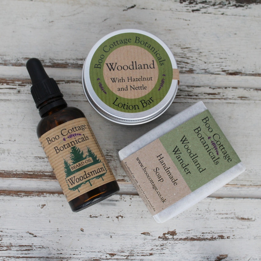 Beard oil in amber bottle with black dropper pipette, soap bar and lotion bar in aluminium round tin all with green labels on whitewashed wooden background