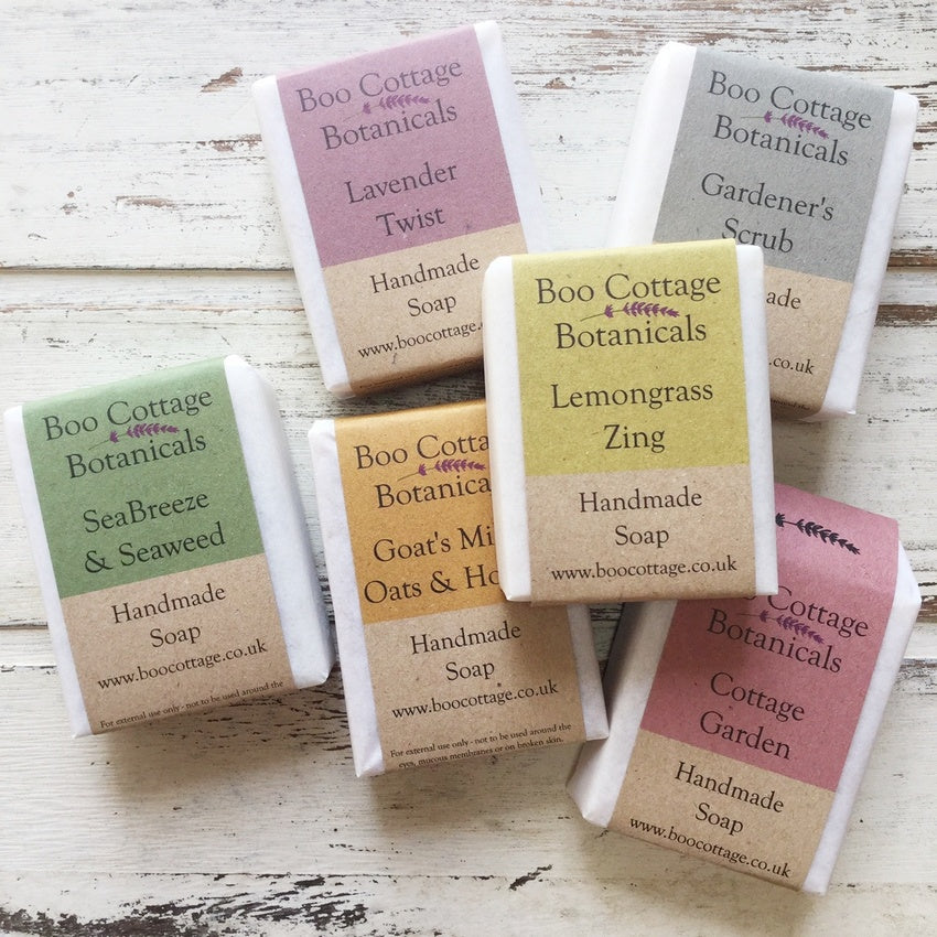 Six bars of different natural soap wrapped in multicoloured card on white wood background